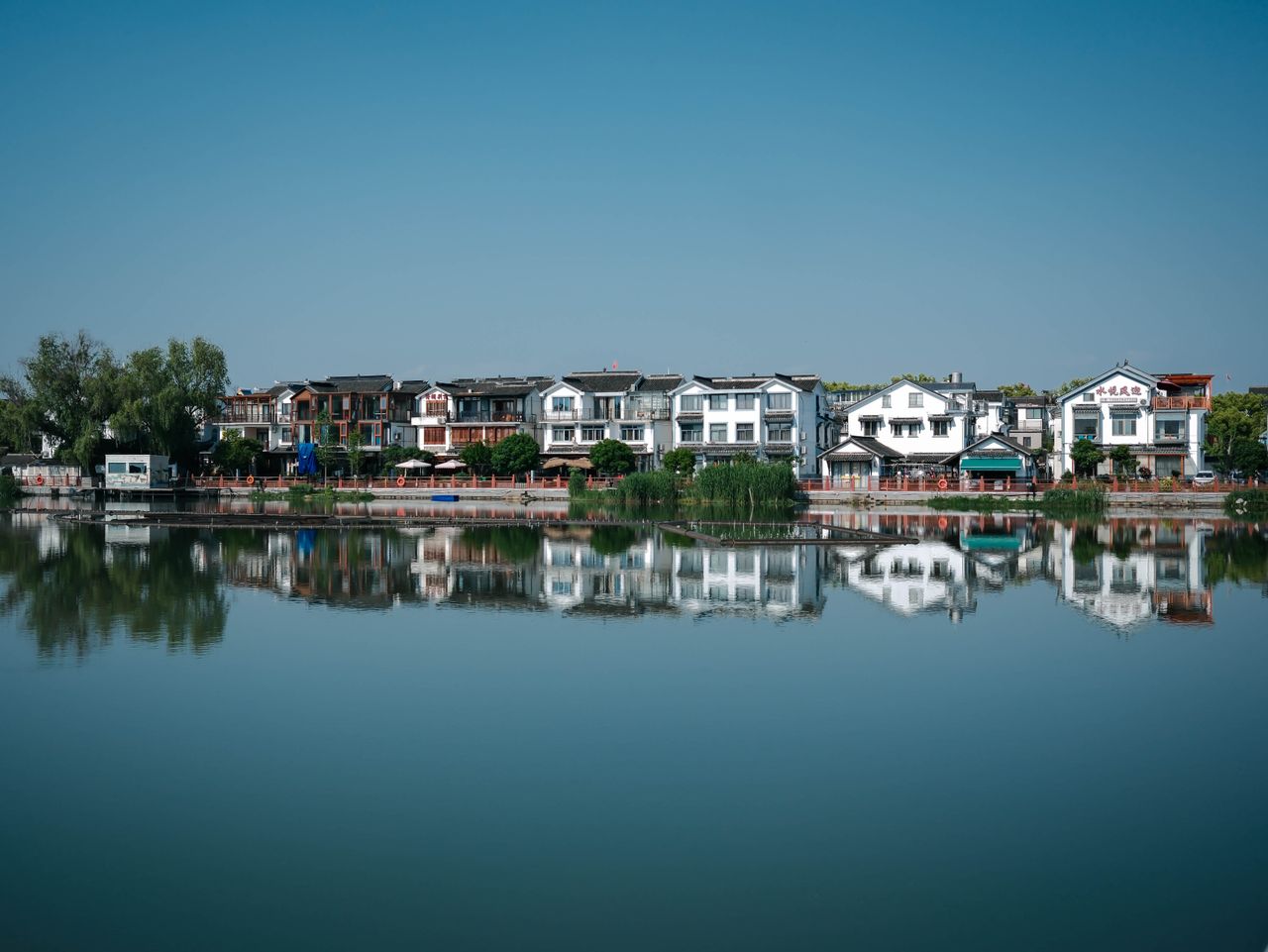 Charming traditional homes reflecting in calm lake waters under a clear blue sky.